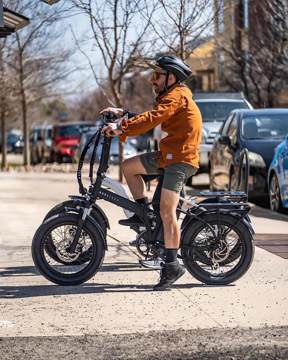 A cyclist wearing a helmet rides a MOD City+ foldable electric bike in an urban setting.