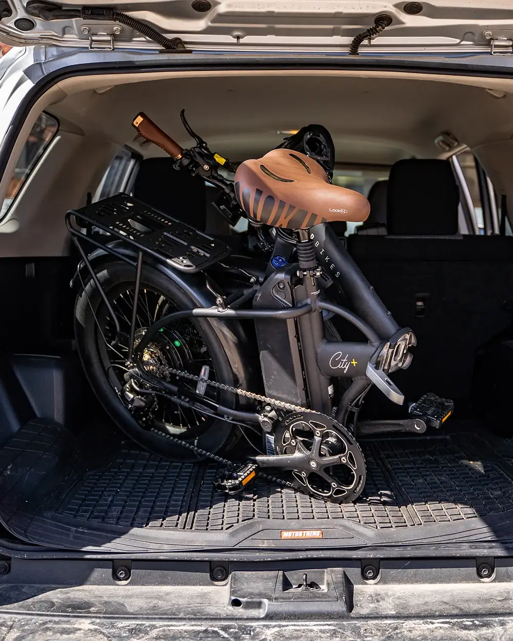 Foldable MOD City+ electric bike stored in a car trunk, showcasing its compact design and lightweight features.