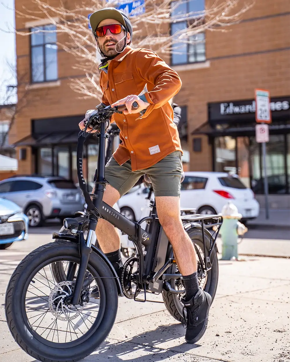 Man riding MOD City+ 3 foldable electric bike in urban setting, showcasing its stylish design and full-suspension features.