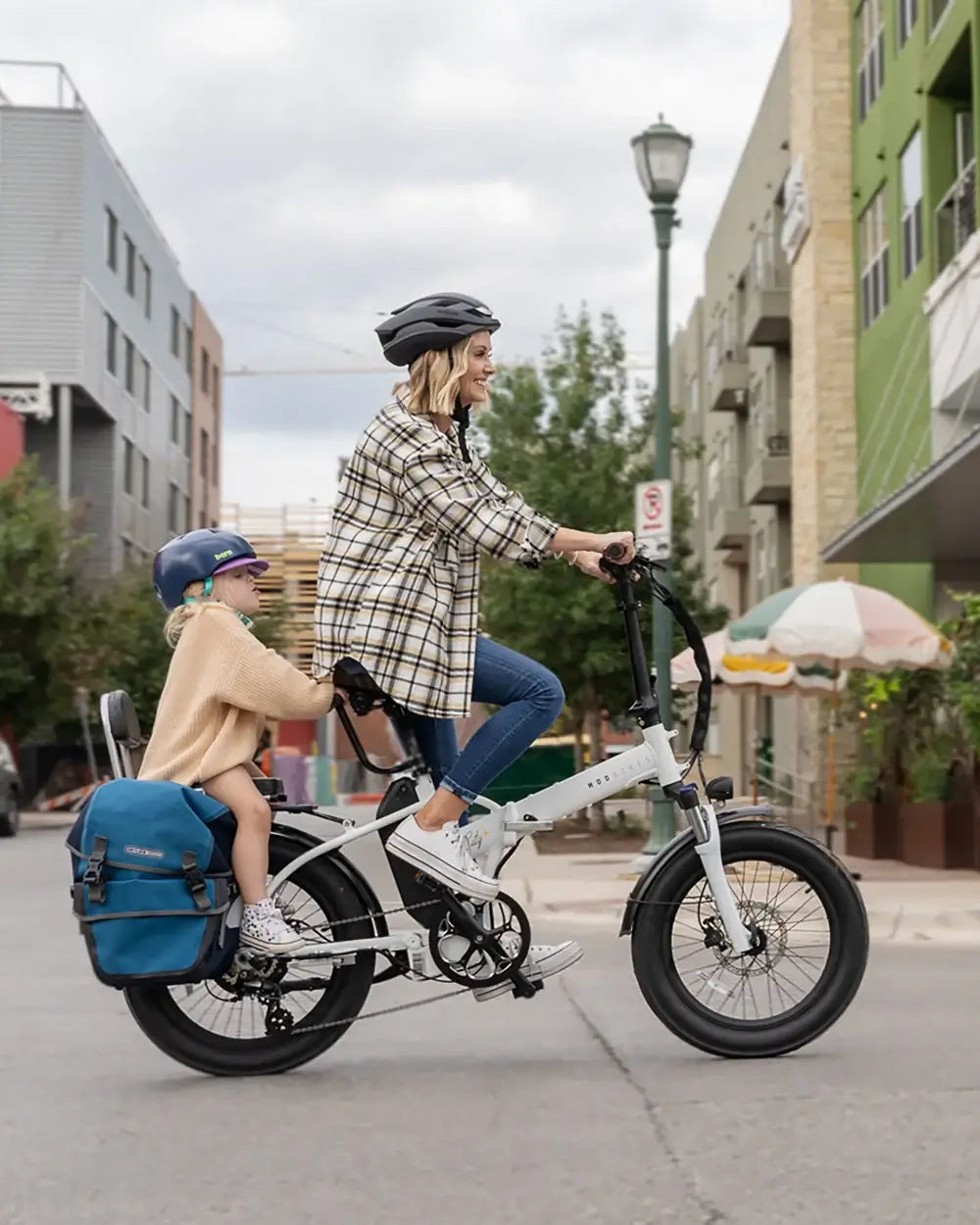 Woman riding MOD City+ foldable electric bike with child, showcasing urban adventure and family-friendly features.