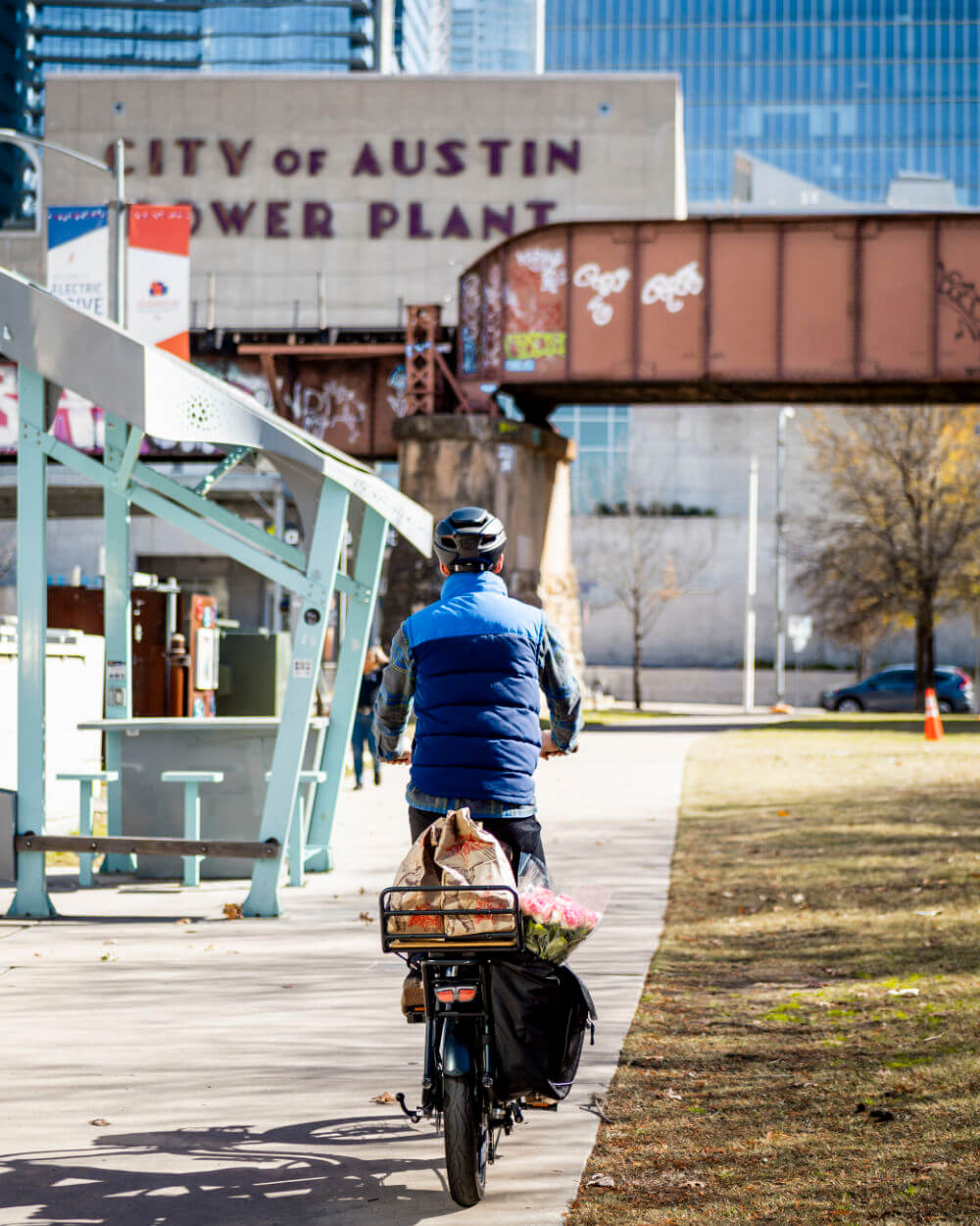 Cyclist on a path near Austin Power Plant with cargo bike loaded with groceries, showcasing urban transportation ease and practicality.