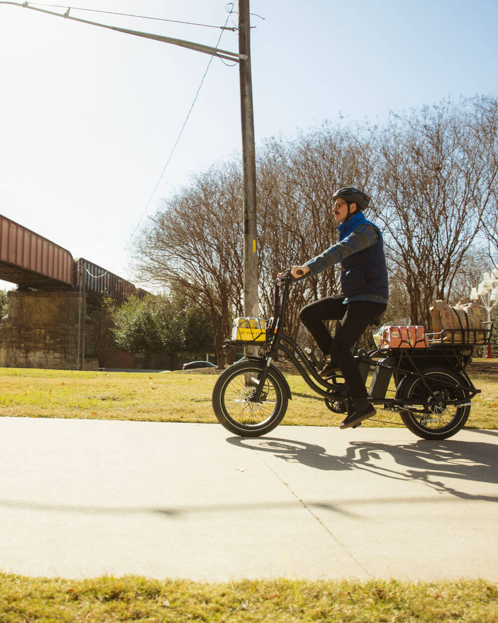 Person riding MOD CarGo 3 electric bike with Snap-On rack, showcasing its hauling capability on a sunny day.