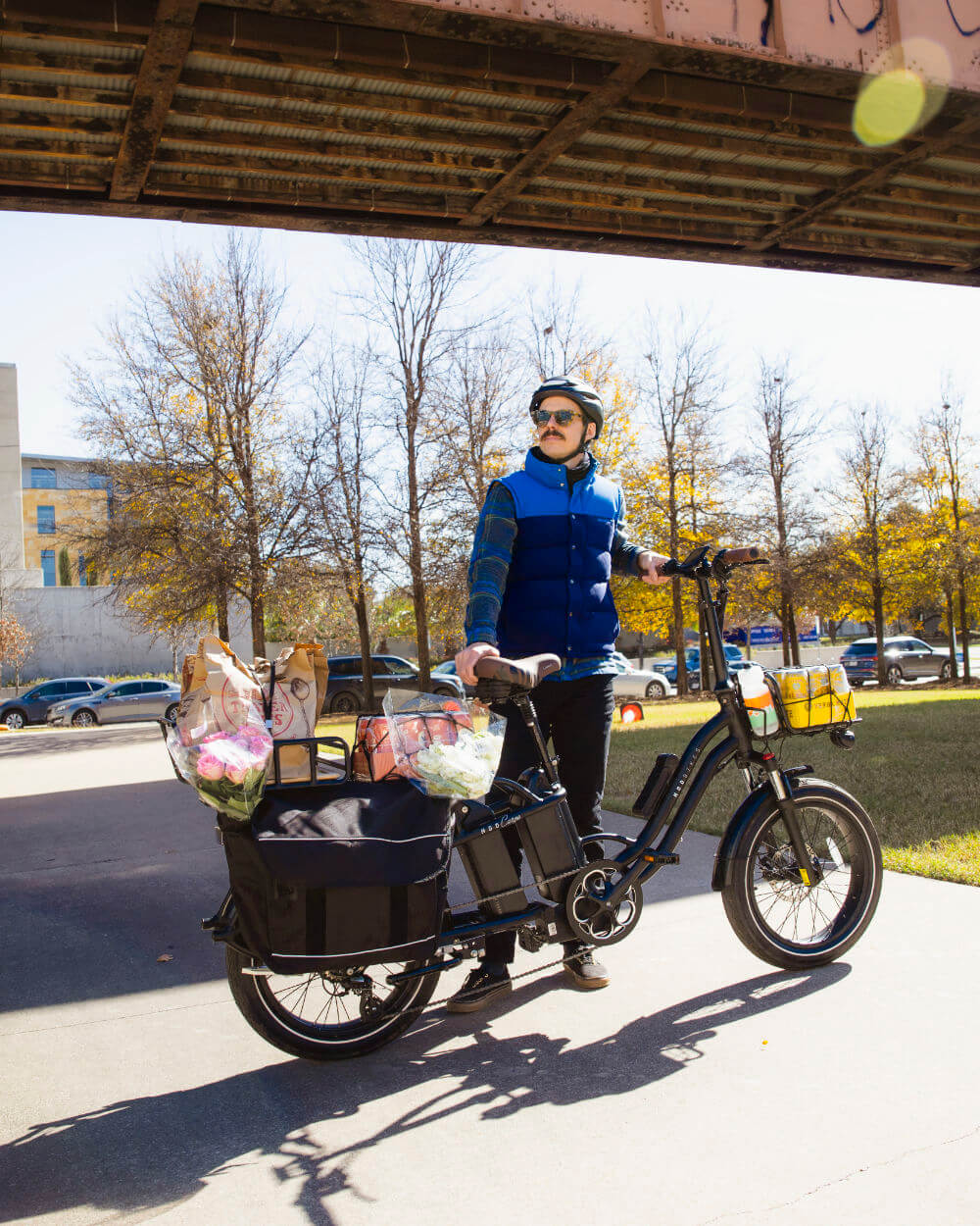 Person riding MOD CarGo 3, a versatile bike with Snap-On rack and groceries, in a park under a bridge.